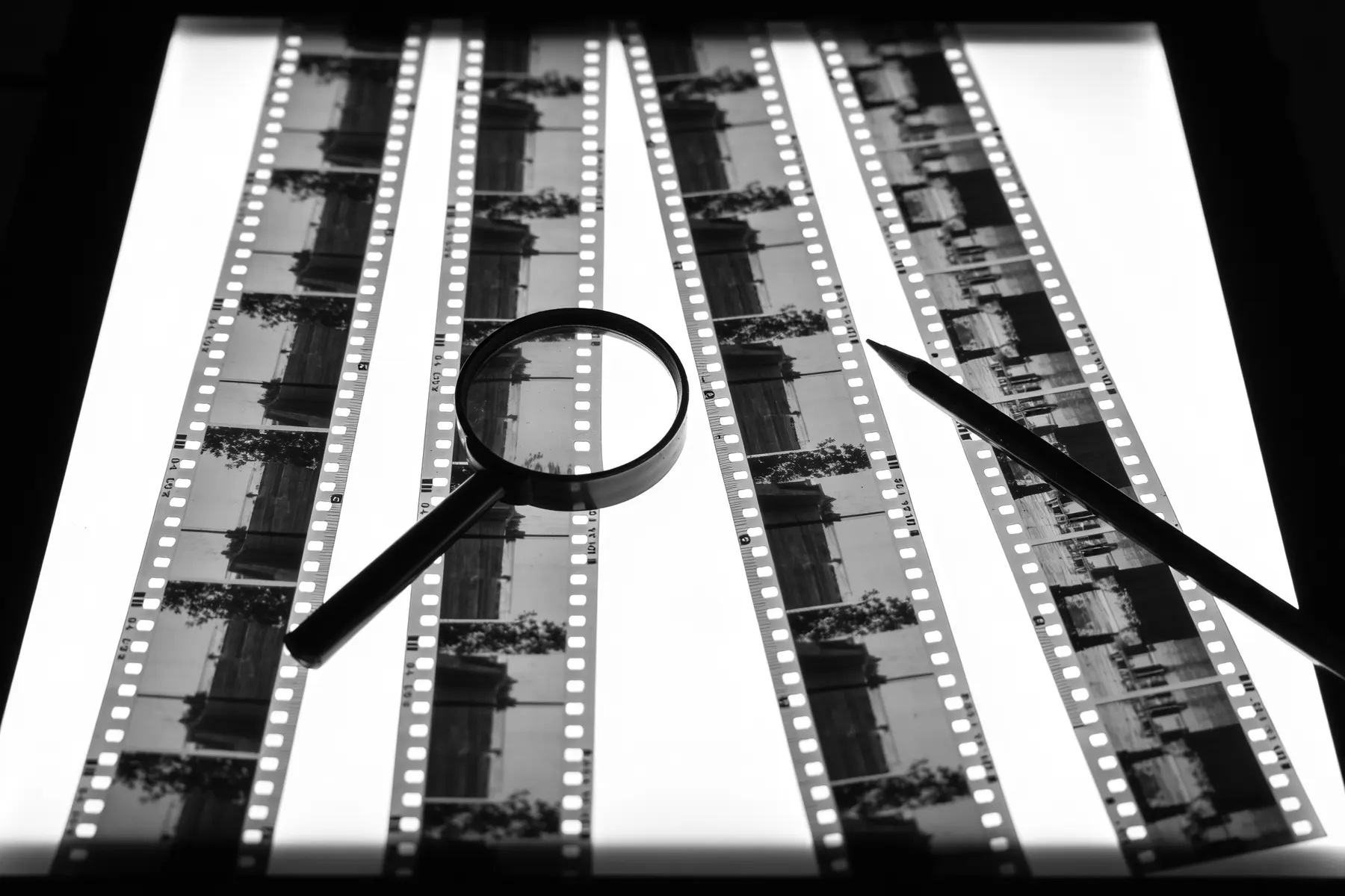 Four strips of 35 mm negatives on a lightbox with a loupe beside them